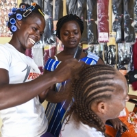 A woman braids the hair of another woman while a third woman watches on