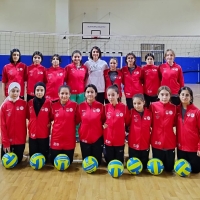 Girls pose on a volley ball court and smile to the camera