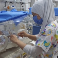 A woman wearing a mask is working in a neonatal intensive care unit.