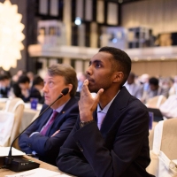 Sitting at a desk at the conference, Nour Mussa is looking slightly upwards, as though listening to a speaker who is not in the photo, his hand on his face looking thoughtful.