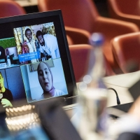A view from over the shoulder of the High Commissioner, who is looking at screens of virtual participants