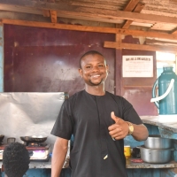 A man standing in a restaurant kitchen. He is smiling and giving a thumbs up to the camera