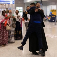 Father Solomon embraces tightly his youngest son, Yoftahie, who has just landed to Athens with his mother and siblings under the gaze of female members of the Eritrean Orthodox congregation in Greece, who joined Father Solomon welcoming his family at the International Airport of Athens
