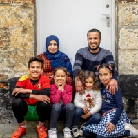 A family sitting on a porch, smiling and facing the camera