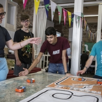 A group of youths working together to makes toy cars move.