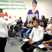 People seated listening to a woman talking in front of them.