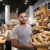 A baker stands with showing a basket of bread behind a shop counter
