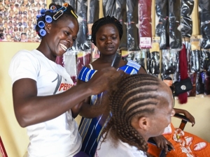 A woman braids the hair of another woman while a third woman watches on