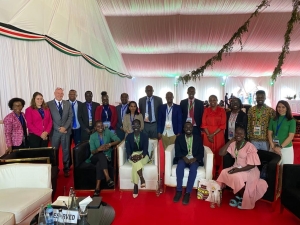 A group photo of refugee participants and UNHCR staff. Some are sitting in armchairs, others standing behind, all smiling and looking at the camera