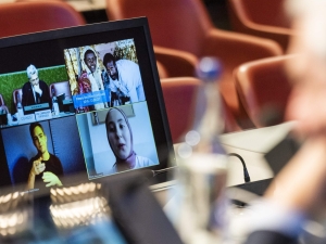 A view from over the shoulder of the High Commissioner, who is looking at screens of virtual participants