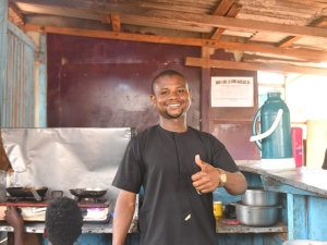 A man standing in a restaurant kitchen. He is smiling and giving a thumbs up to the camera
