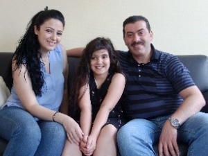 A woman, man and a child smiling at the camera sitting in a couch.