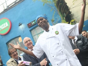 A chef standing with his hands up and smiling, while others clap.