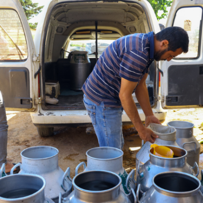 Two men in front of a van with milk cans