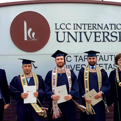 Students smile at the camera. They are holding their diplomas and are wearing graduations caps and gowns.