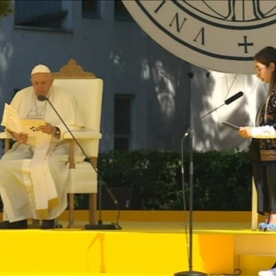A woman giving a speech on a stage, with the pope also speaking next to her