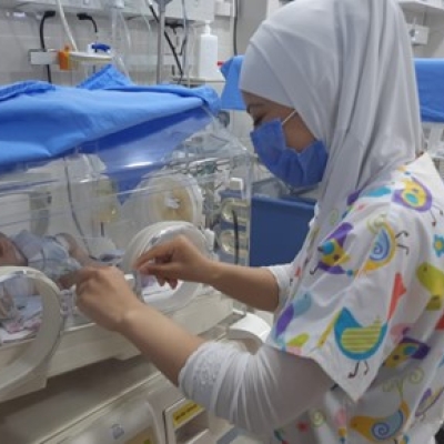 A woman wearing a mask is working in a neonatal intensive care unit.