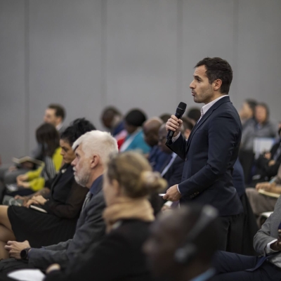 A man standing up in the audience of an event, speaking into a microphone