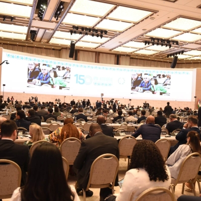 A wide-angle photo of the assembly from behind, showing participants and screens in the distance
