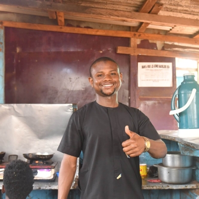 A man standing in a restaurant kitchen. He is smiling and giving a thumbs up to the camera