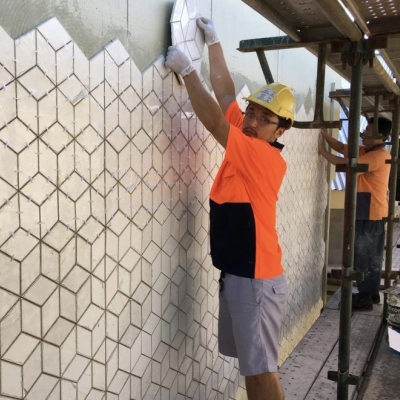 Man placing a tile in wall.