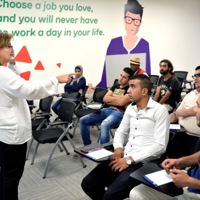 People seated listening to a woman talking in front of them.