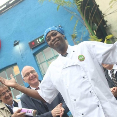 A chef standing with his hands up and smiling, while others clap.