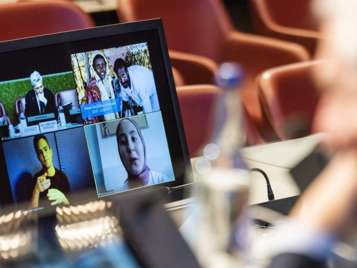 A view from over the shoulder of the High Commissioner, who is looking at screens of virtual participants