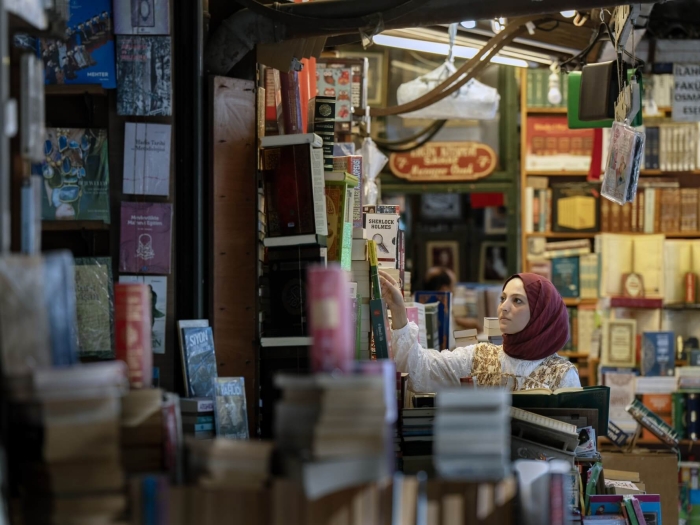 A woman in a bookshop or library reaching up to look at a book
