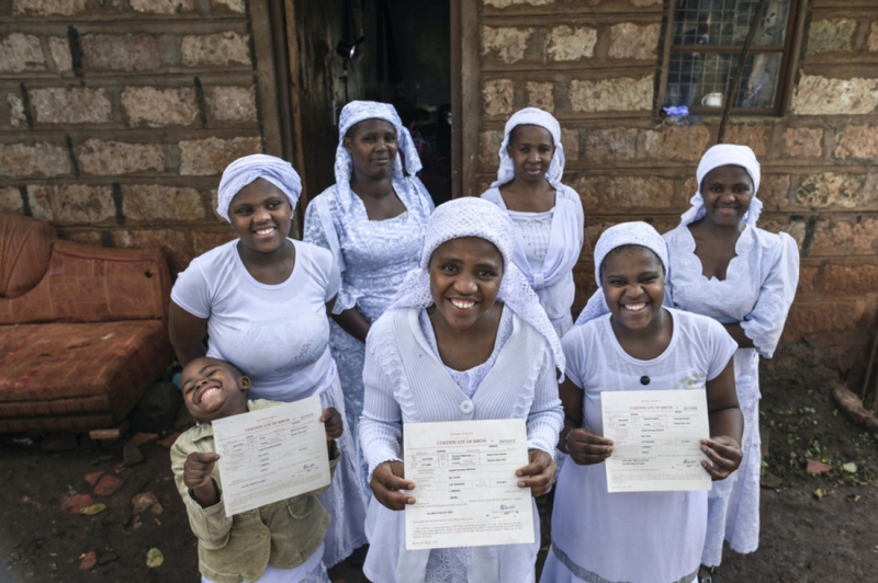 A group of people face the camera smiling holding up birth certificates
