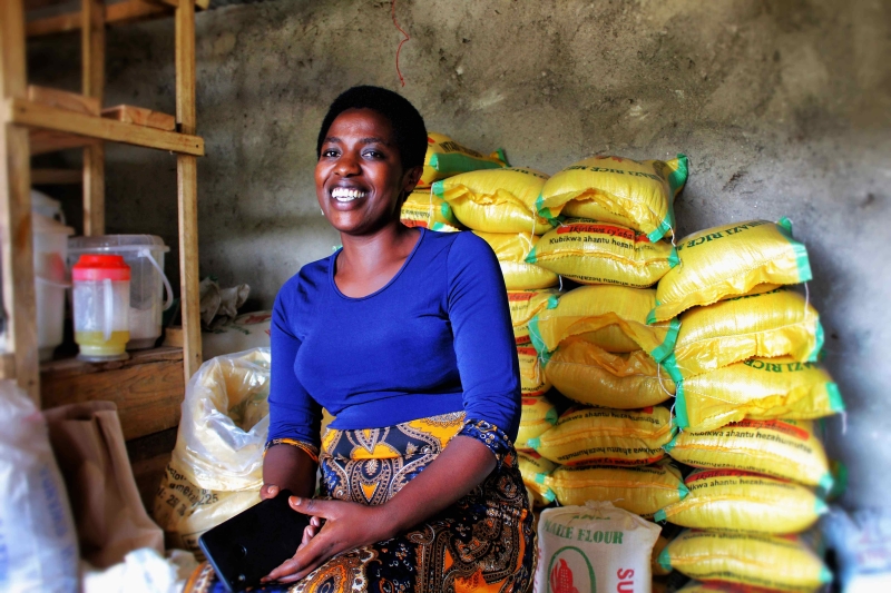 A woman sits in front of bags of rice smiling