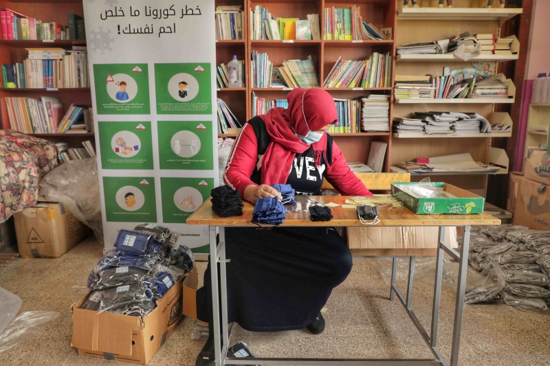 A woman is sitting at a desk. There are masks on the desk and boxes of packages masks on the floor.