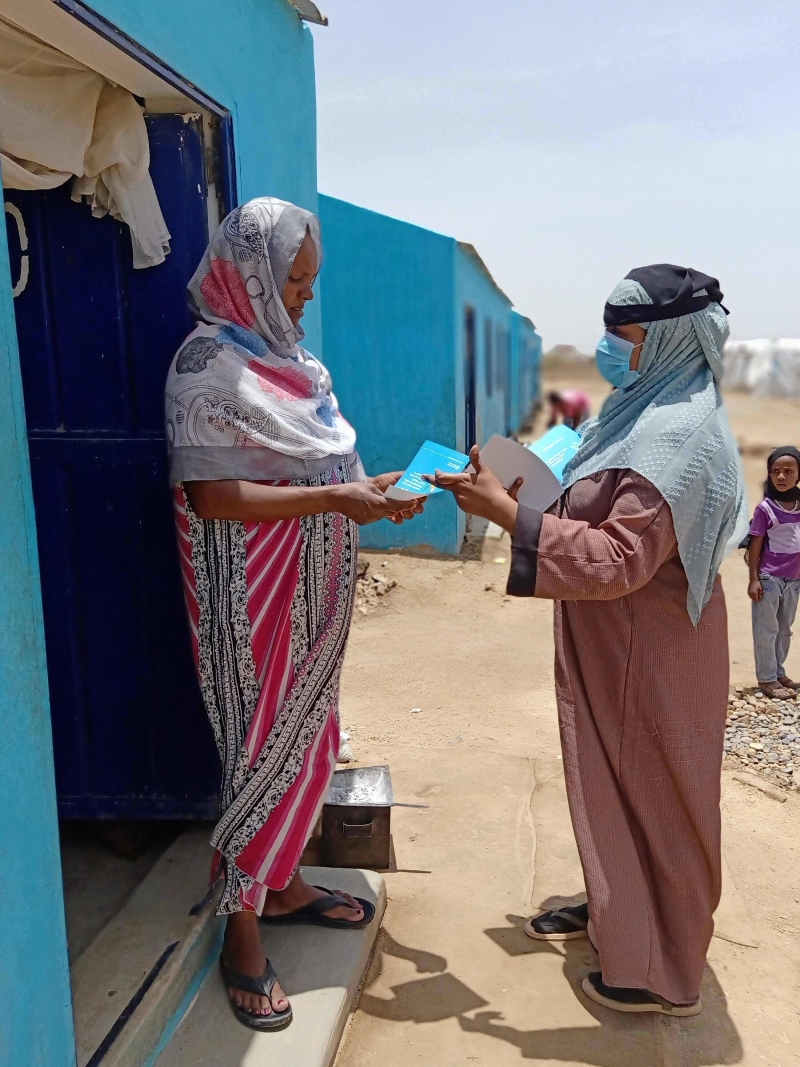A woman wearing a mask hands out a flyer to another woman.