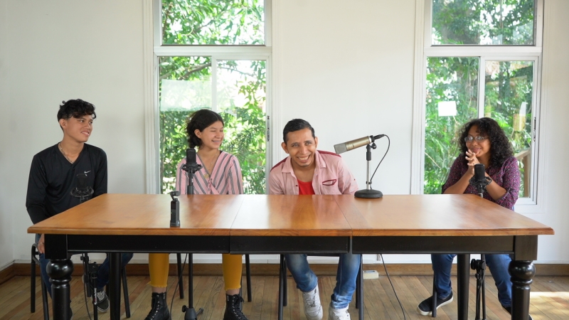 A group of four young people sit at a table with microphones