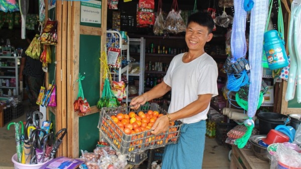 A man standing in front of a shop holding a tray of oranges