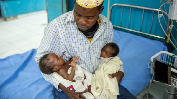 A man holding two new born babies in a hospital