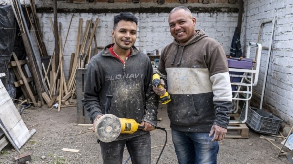 Two men on a construction site holding power tools and smiling at the camera