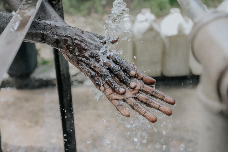 A person washing their hands under running water - only the hands and water are visible