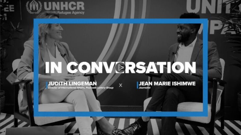 Video still showing the two participants sitting in arm chairs facing one another, smiling, with their names and the words "In conversation" overlaid