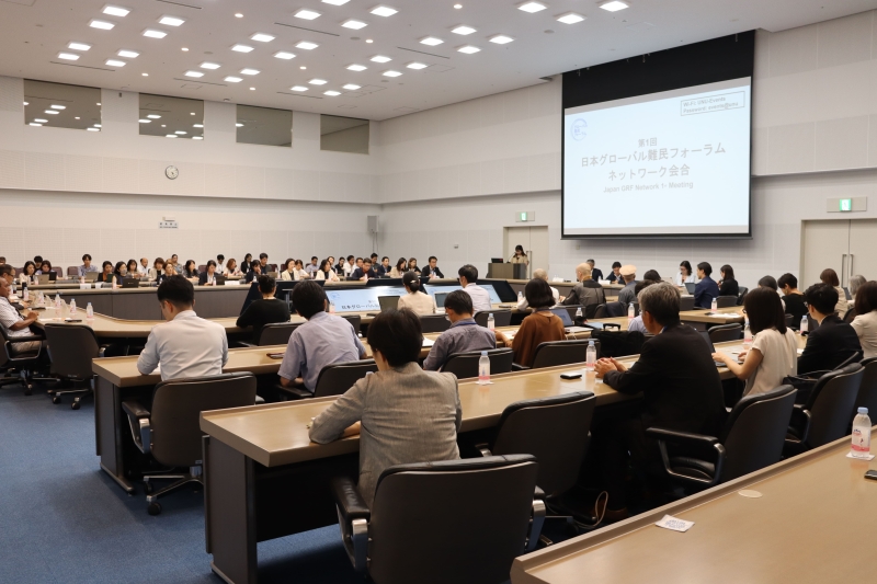 Picture form the back of a meeting room. People are sitting in the room and on the panel.