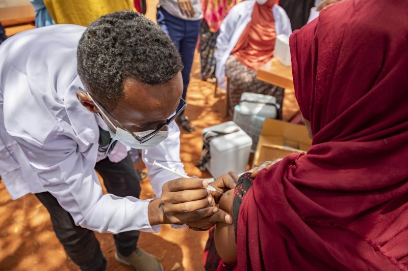 A doctor leaning forwards and giving a vaccination to a woman in her upper arm
