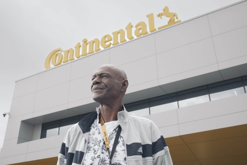 A man standing in front of a building with a sign saying "Continental" on top of it. He is looking off into the distance, and the camera is angled below him, so the top of the building and sky are visible above