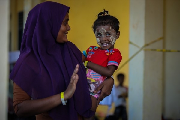 a woman holding a young child who is wearing face paint. They are both smiling, and the woman is offering the child a high five
