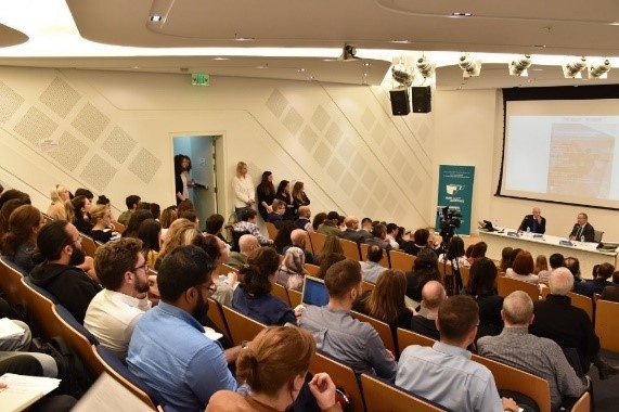 People at a conference room, seated facing the podium.