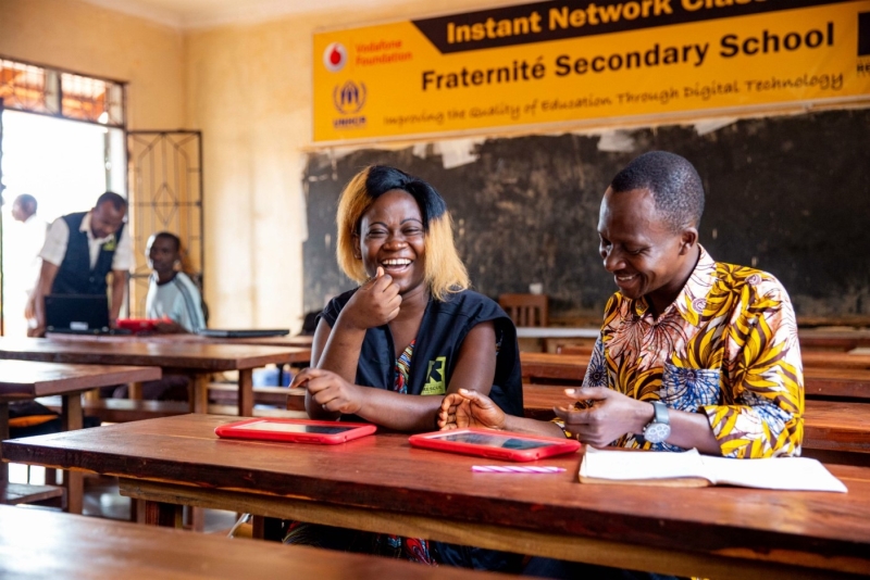 Volunteers sitting at desks in a classroom looking over tablets and laughing