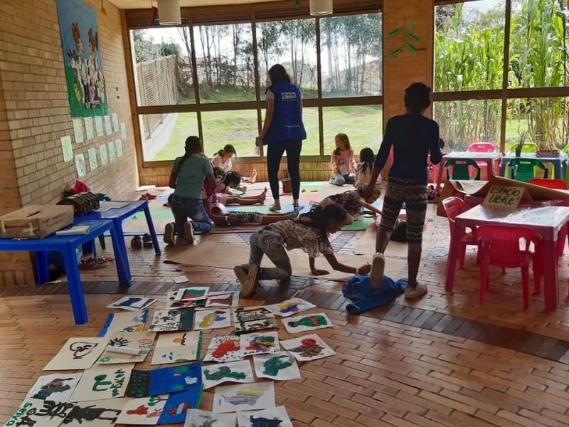 Children playing and drawing under the supervision of a woman.