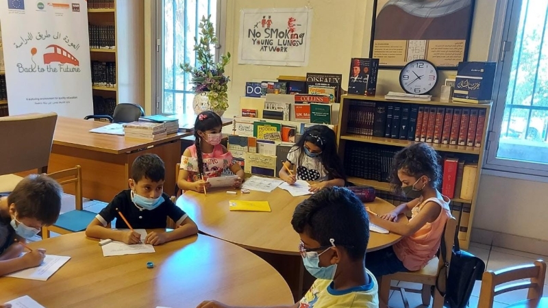 Children wearing masks sitting at a table writting