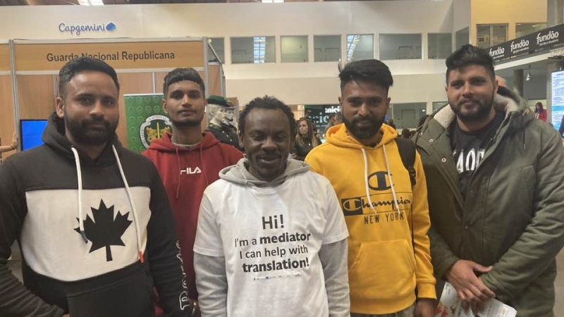A group of men pose for the camera - one is wearing a shirt that say "Hi! I'm a mediator. I can help with translation"