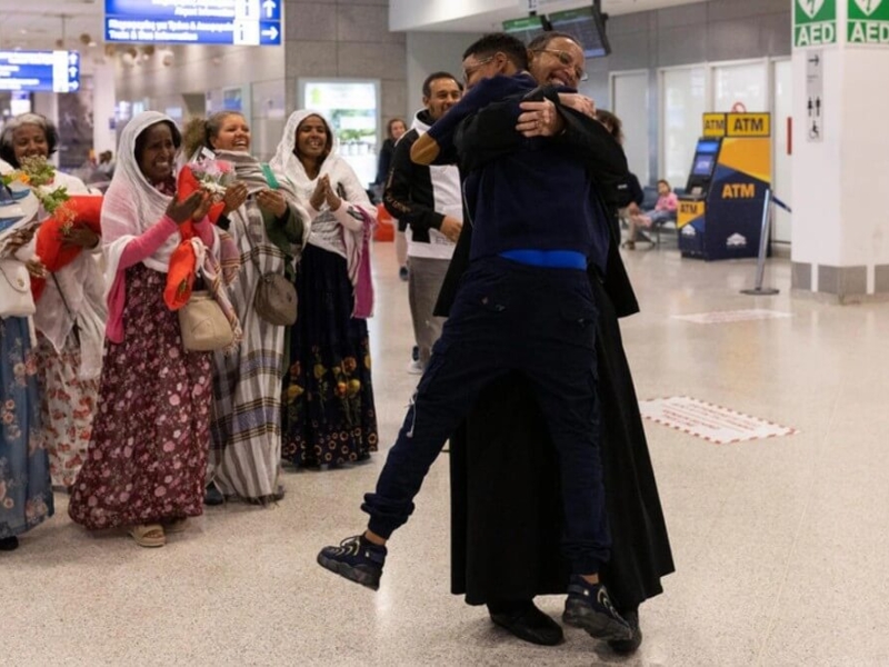 Father Solomon embraces tightly his youngest son, Yoftahie, who has just landed to Athens with his mother and siblings under the gaze of female members of the Eritrean Orthodox congregation in Greece, who joined Father Solomon welcoming his family at the International Airport of Athens