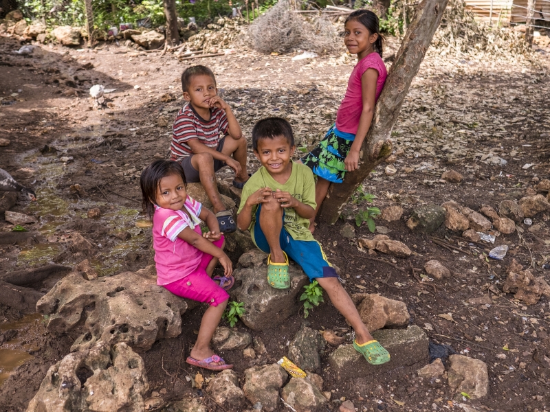 Four children play outside and smile for the camera.